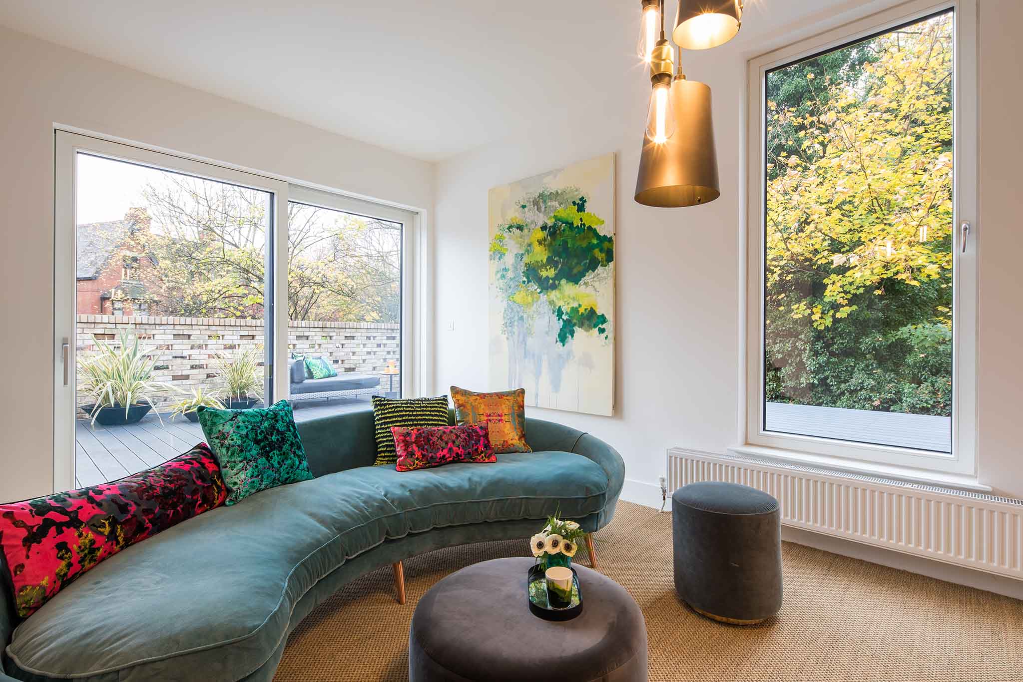 Modern living room with a curved sofa, colourful cushions, and large triple-glazed windows.