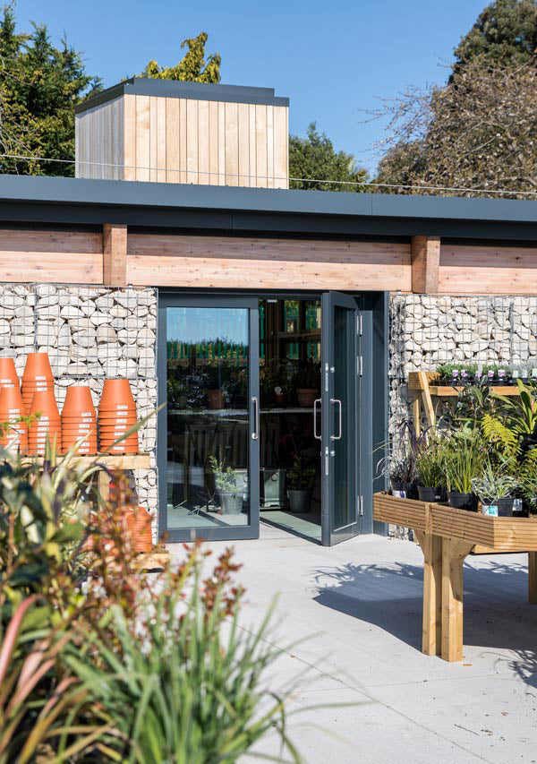 Modern garden building with triple-glazed glass doors, stone walls, and outdoor furniture.