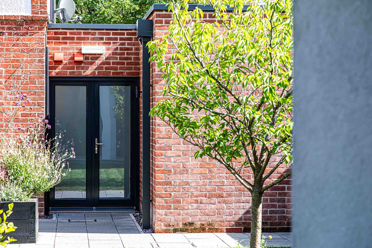 Modern house entrance with a triple-glazed black door and red brick wall