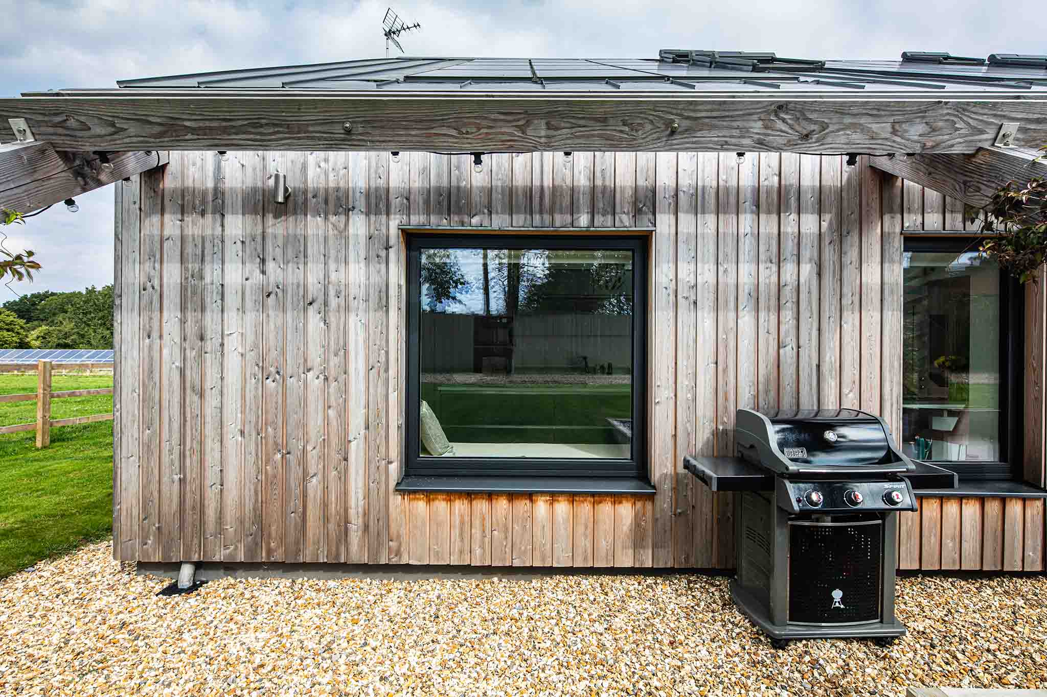 Wooden cabin with triple-glazed windows, a grill in front on a gravel area