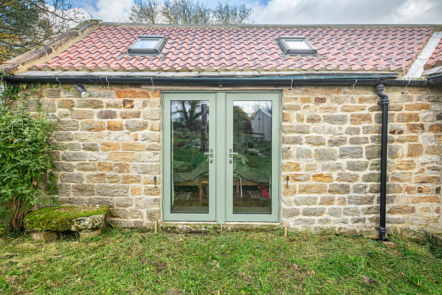 Stone building with a triple-glazed green door and red tiled roof