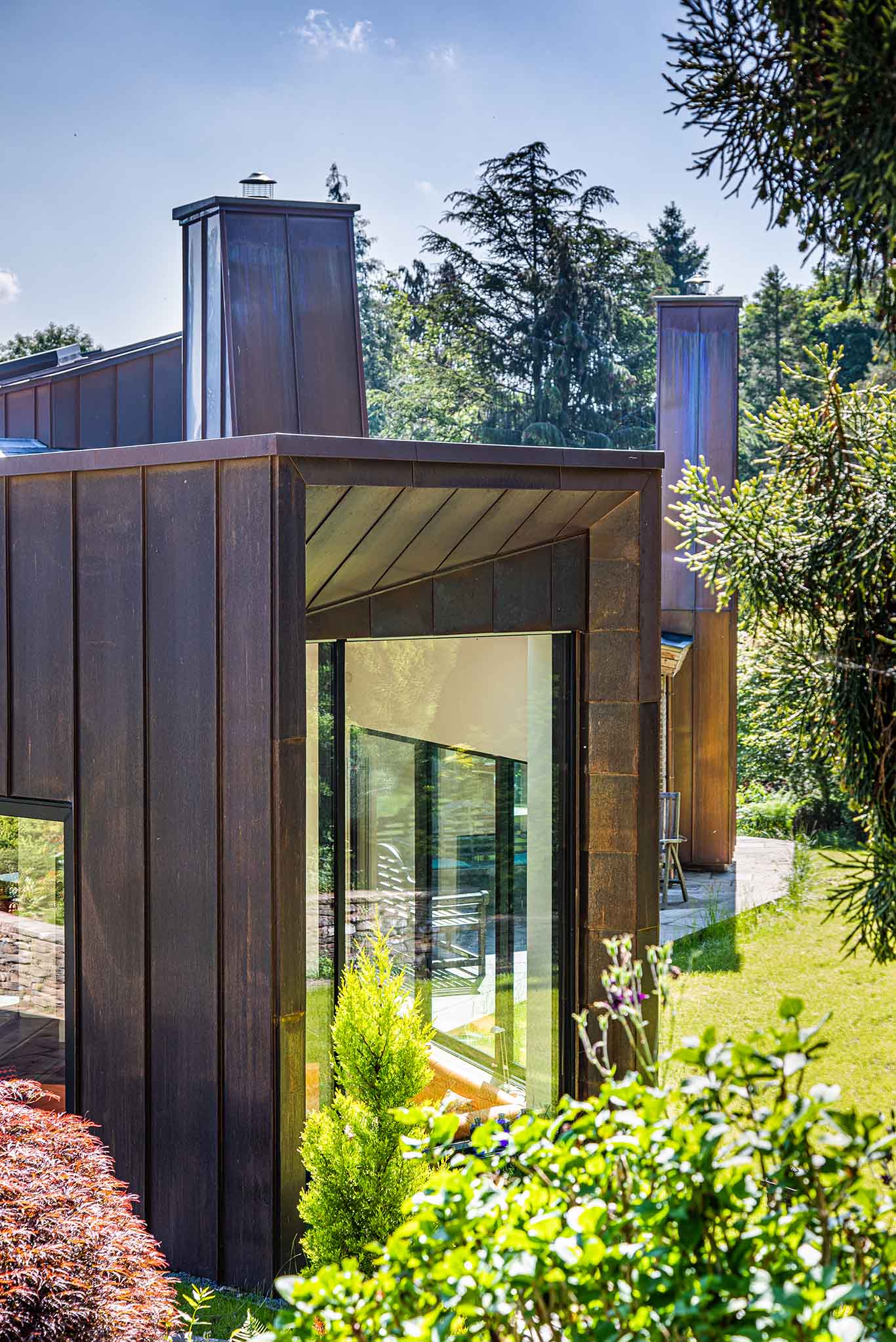 Modern house exterior with triple-glazed glass door and metal facade, surrounded by greenery.