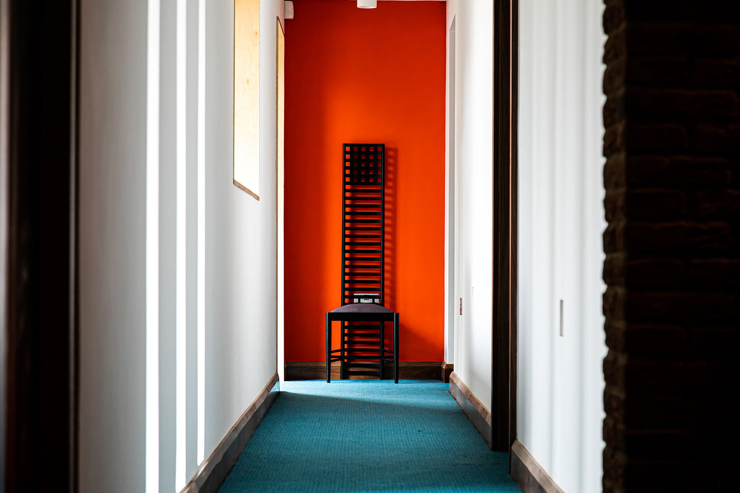 Hallway with a triple-glazed window, red wall and a black chair on a blue carpet