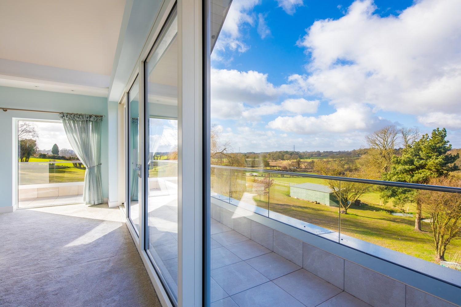 Modern balcony with large double-glazed glass doors and a view of a green landscape.