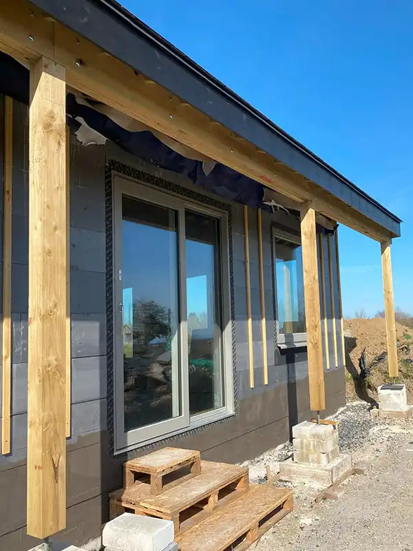 House exterior with triple-glazed windows, wooden pillars and a clear blue sky