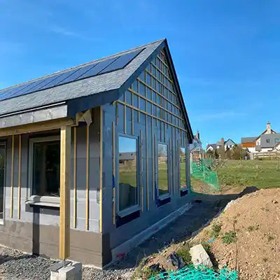 House under construction with triple-glazed windows, solar panels on the roof and a clear blue sky.