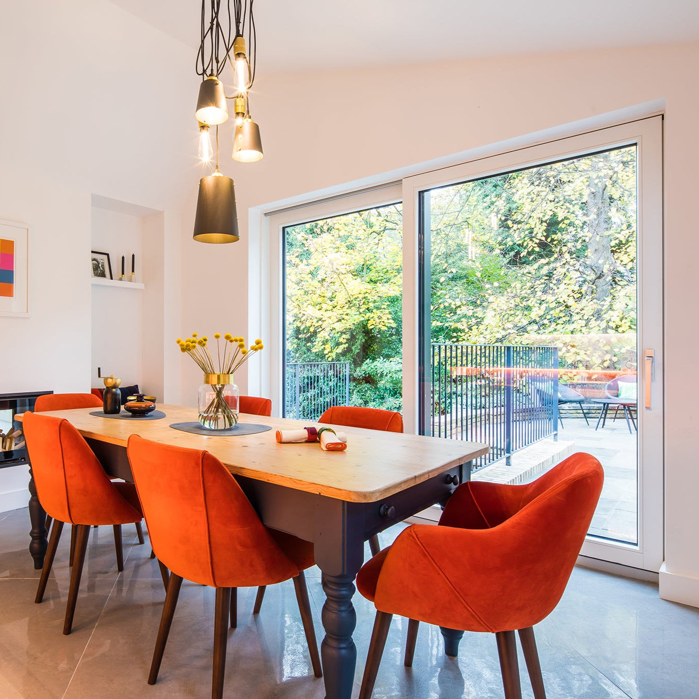 Dining room with a wooden table and orange chairs, large triple-glazed window showing greenery.