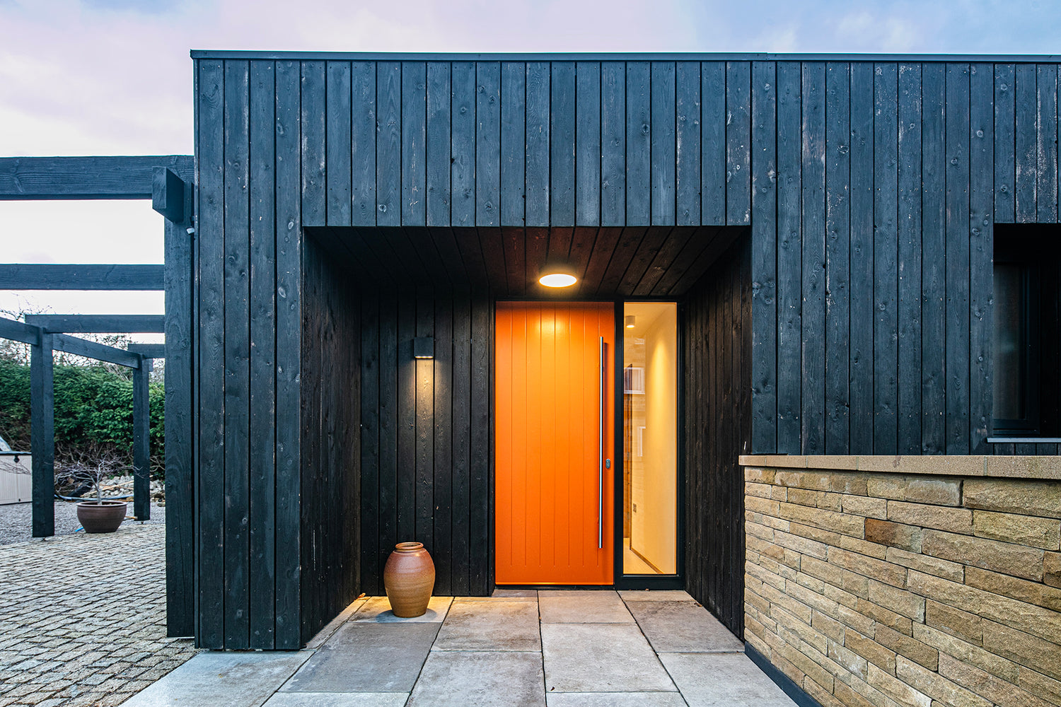 Modern building entrance with dark wooden facade and triple-glazed orange door