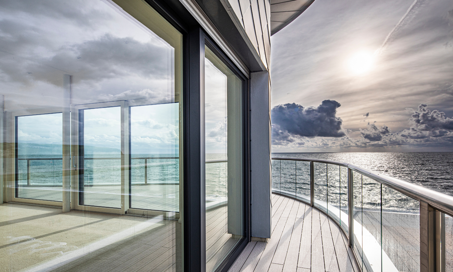 Modern balcony with large triple-glazed glass doors overlooking a body of water.