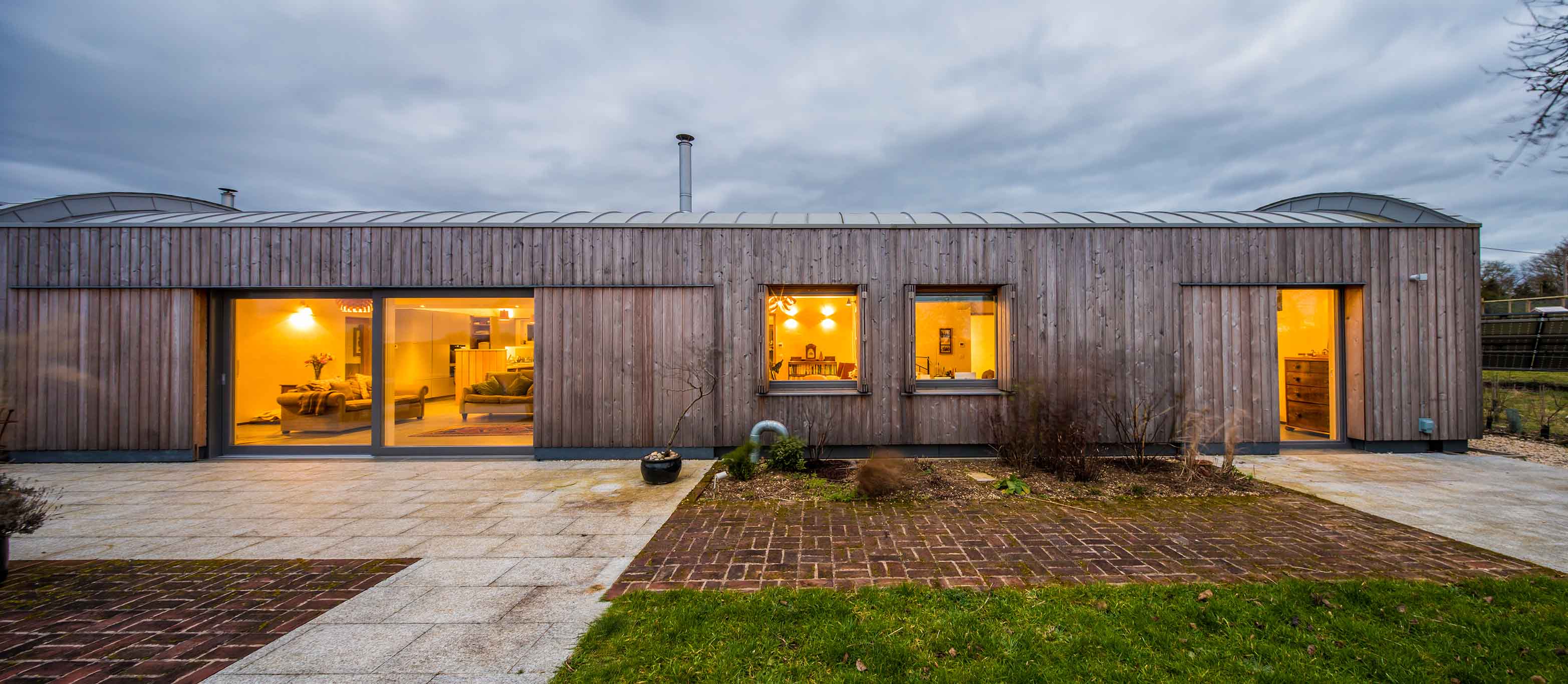 Modern house with wooden exterior and glowing triple-glazed windows on a cloudy day