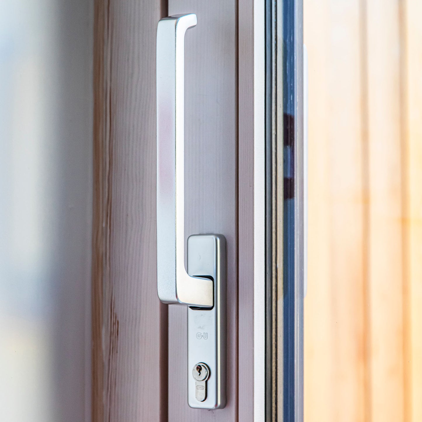 Close-up of a modern door handle on a triple-glazed wooden door with a blurred background