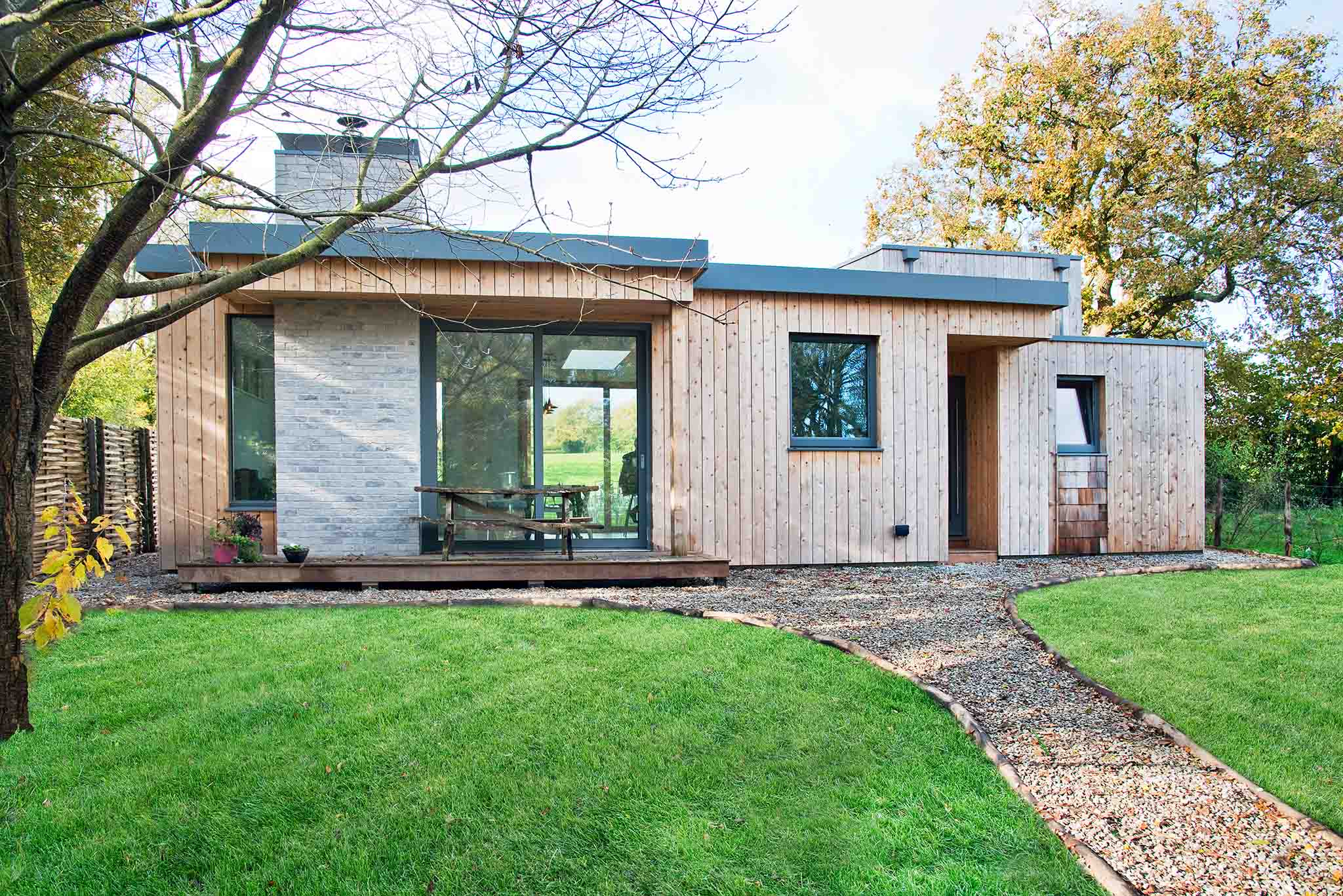 Modern wooden house with large triple-glazed glass windows in a green, tree-lined area