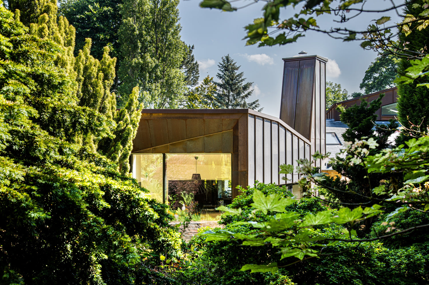 Modern triple-glazed building partially obscured by greenery with a clear sky.