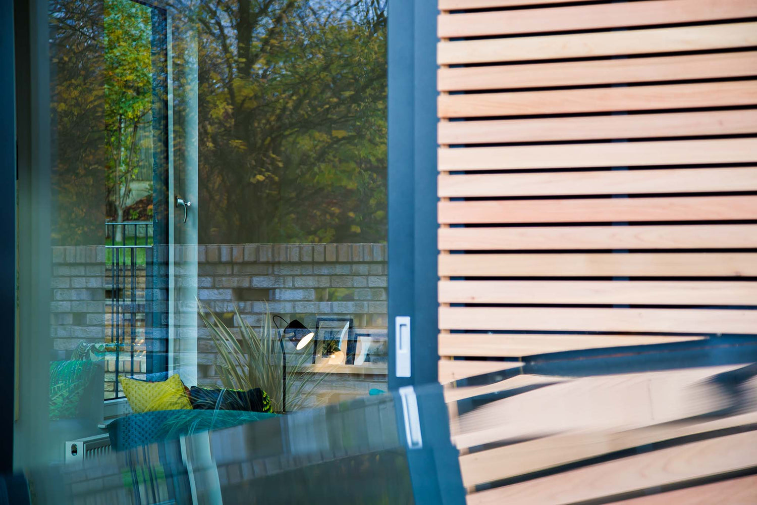 Modern patio with triple-glazed glass door and wooden slat screen, reflecting outdoor garden.