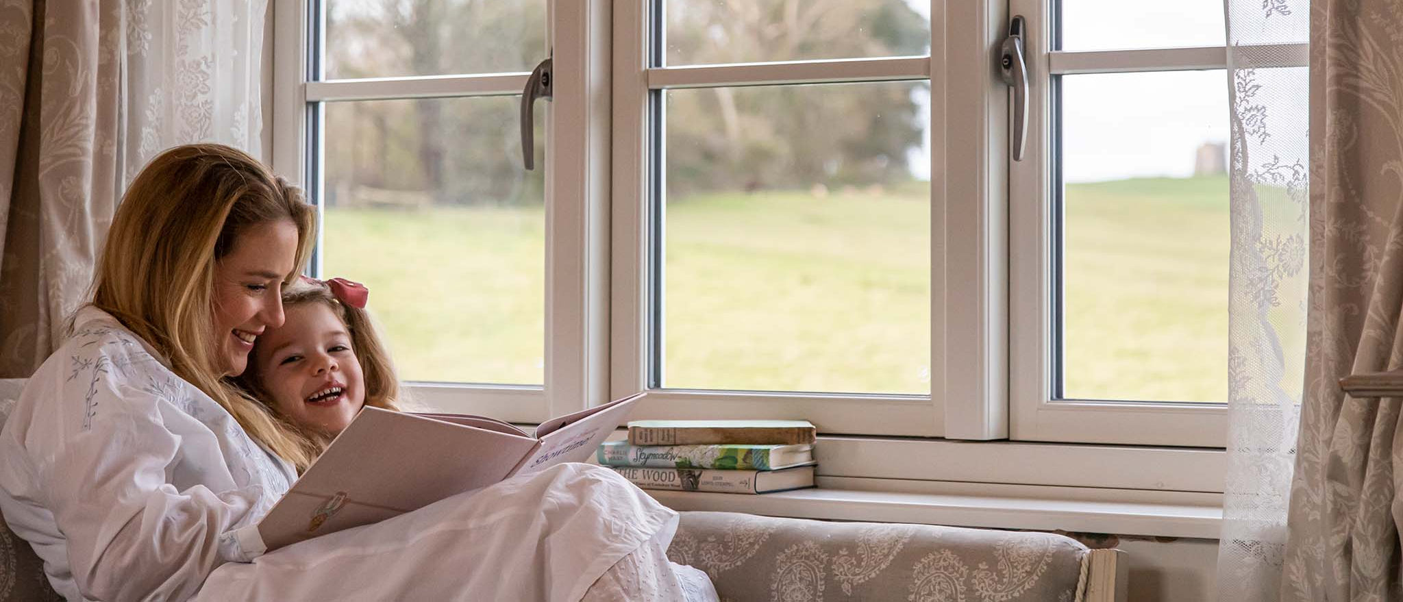 Woman and child reading a book by a triple-glazed window with a view of greenery