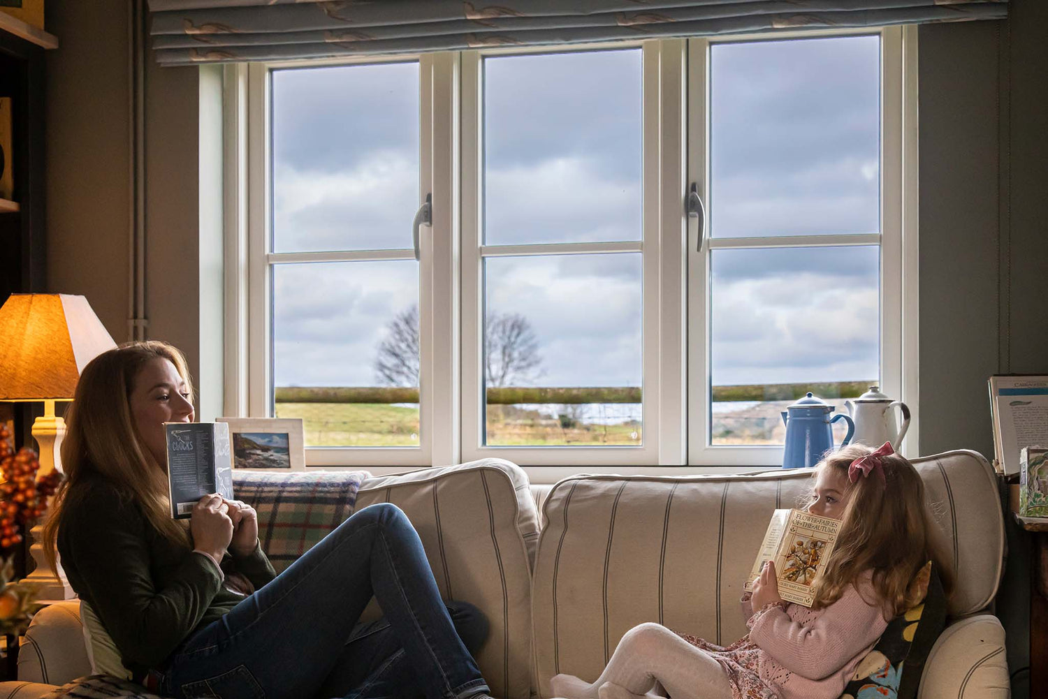 Two women sitting on a couch by a large triple-glazed window, looking out at a scenic view.