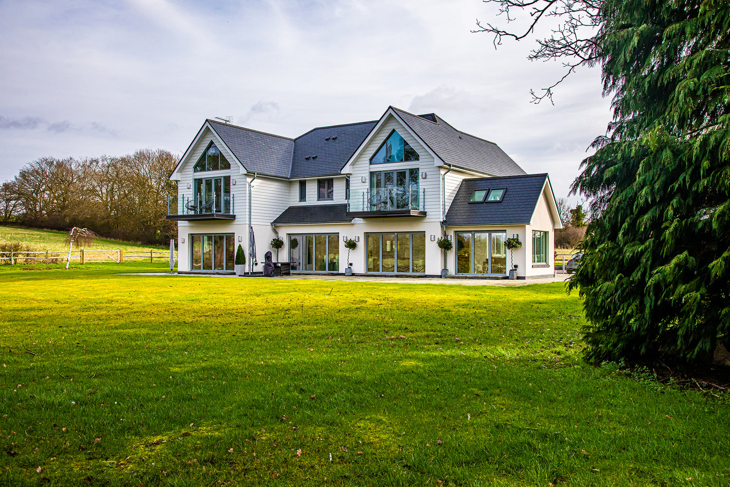 Large, Nordic-style new build home clad in white timber with grey aluminium-clad composite windows and bifold doors in a large open lawn space