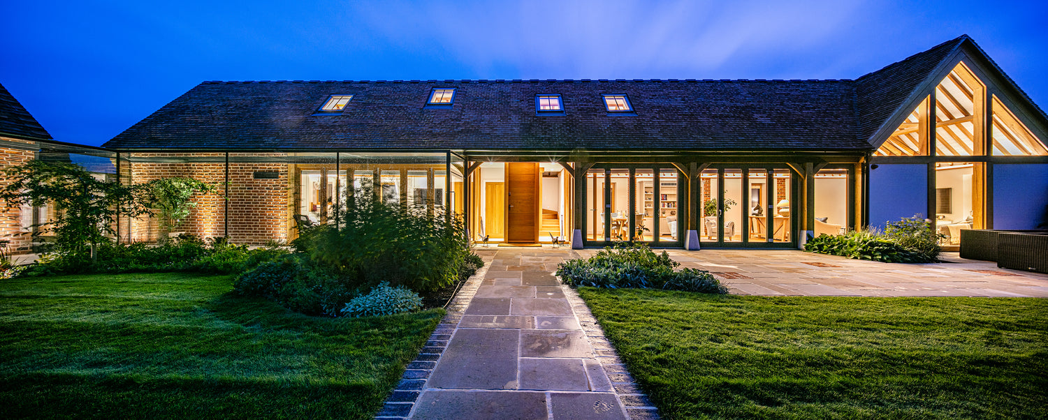 Barn-style building at night with contemporary bifold doors and a large gable installation of triple-glazed windows finished with oak beams