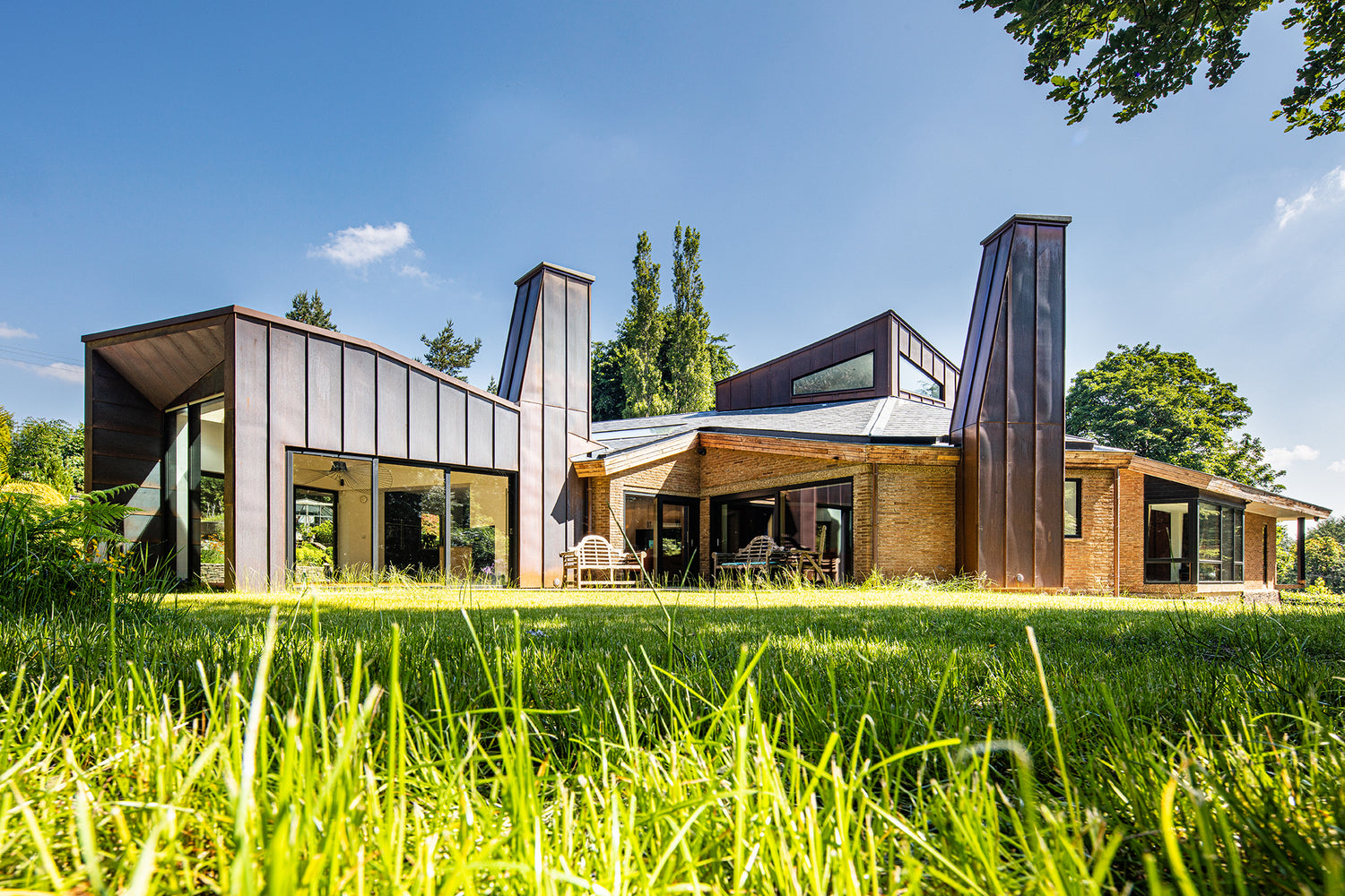 Striking 60s style home in sand-coloured brick with angular extension elements clad in copper and dark coloured composite windows and doors
