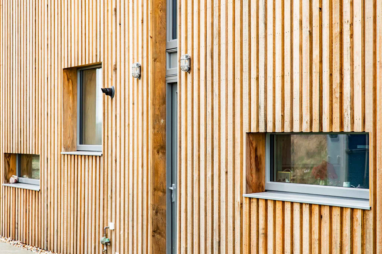 Wooden building exterior with vertical slats and small triple-glazed windows.