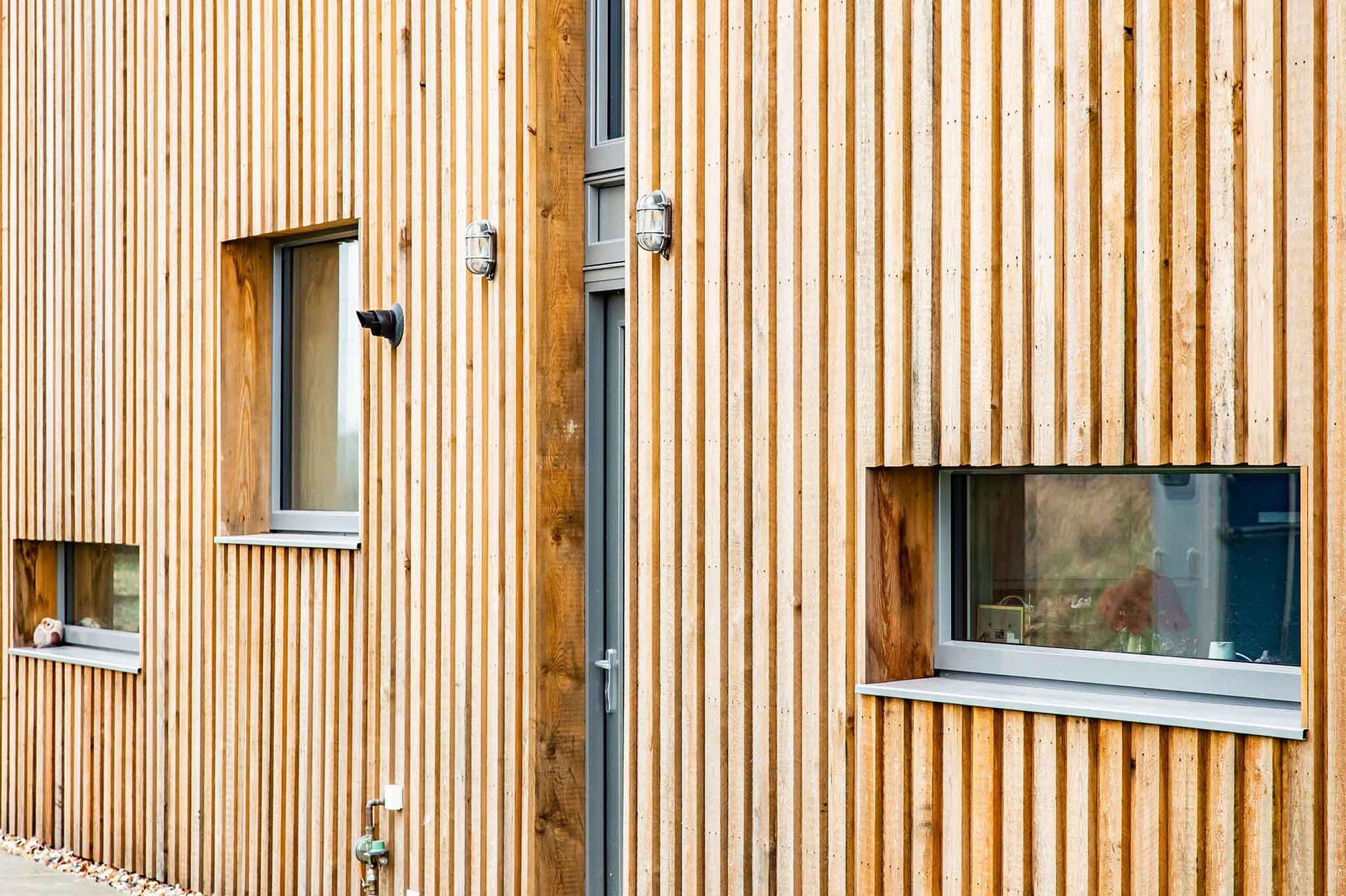 Wooden building exterior with vertical slats and small triple-glazed windows.