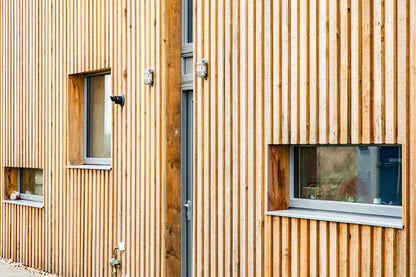 Wooden building exterior with vertical slats and small triple-glazed windows.