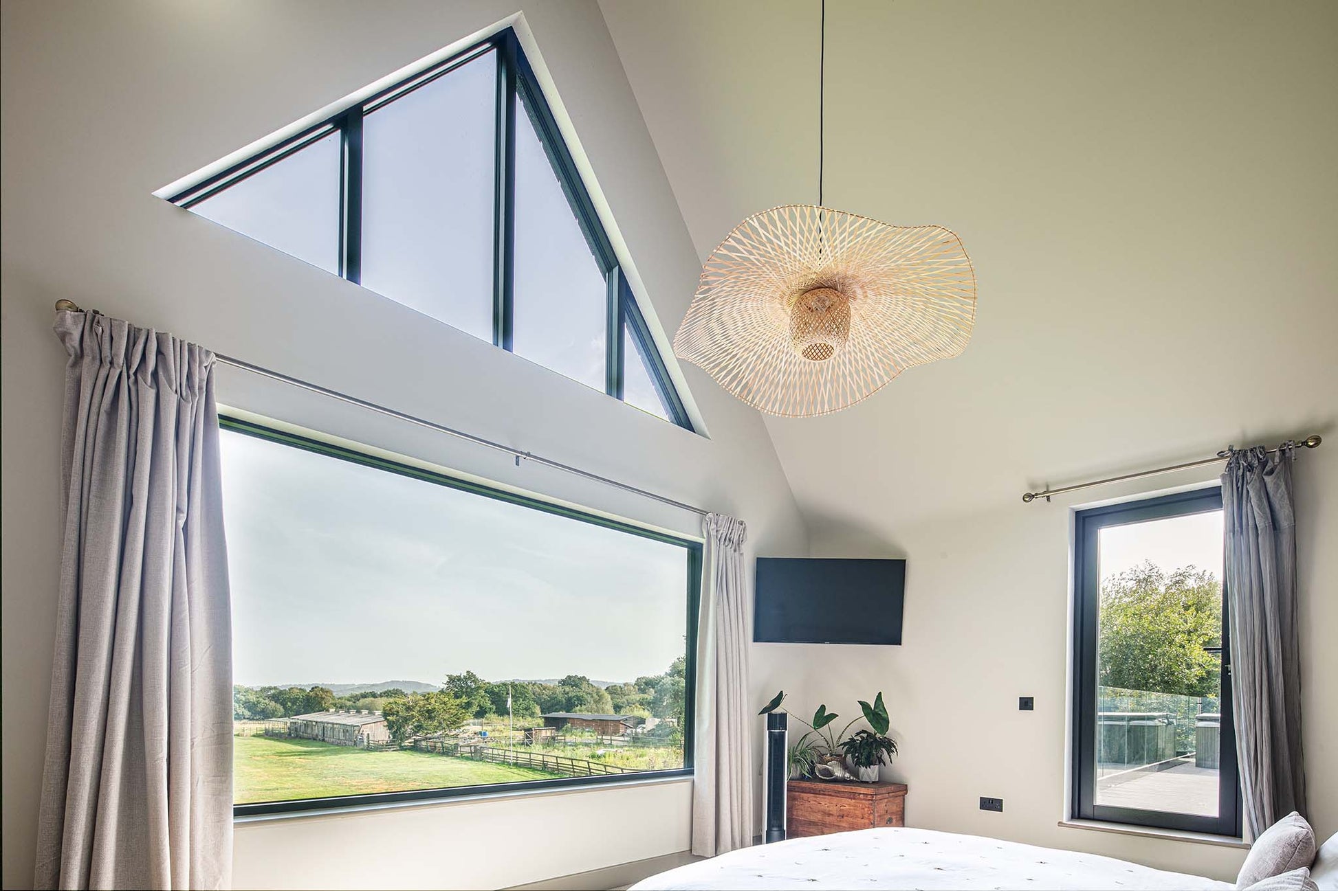 Modern bedroom with large triple-glazed windows, ceiling light fixture, and curtains.