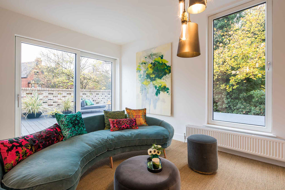 Modern living room with a curved sofa, colourful cushions, and large triple-glazed windows.
