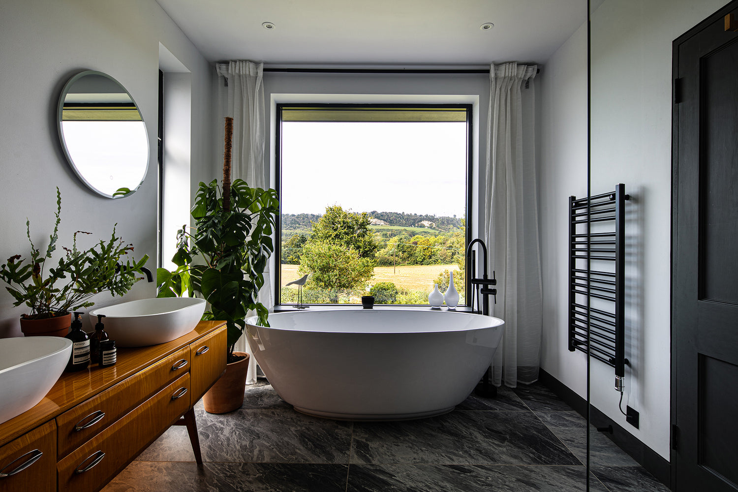 Modern bathroom with a freestanding bathtub, wooden vanity, and large triple-glazed window.