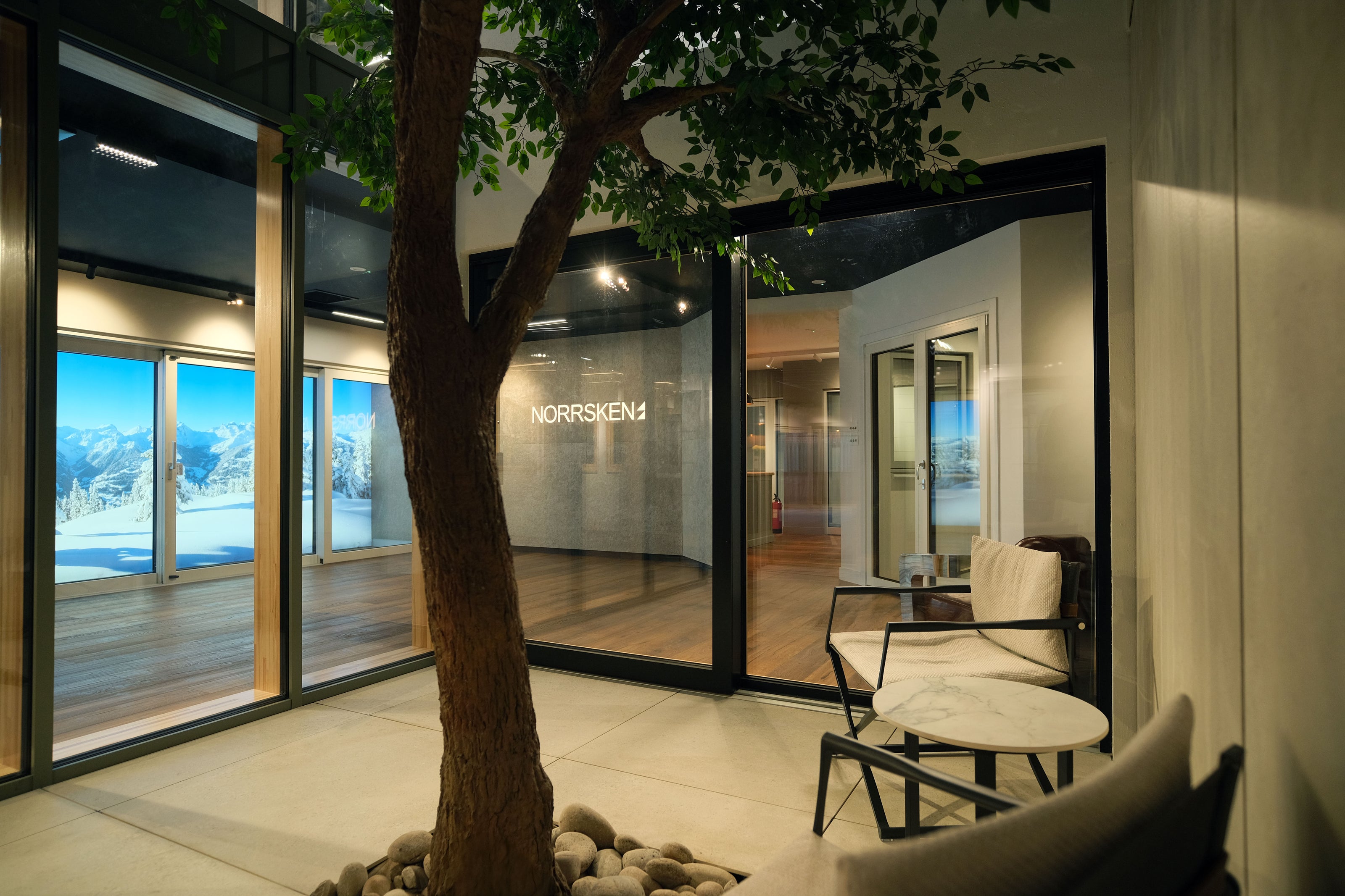 Modern interior design with a tree and  triple-glazed glass walls showing an outdoor view.