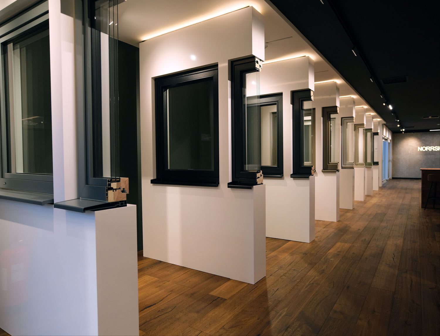 Row of  triple-glazed windows and window cross-sections in white display pods in a modern interior setting.