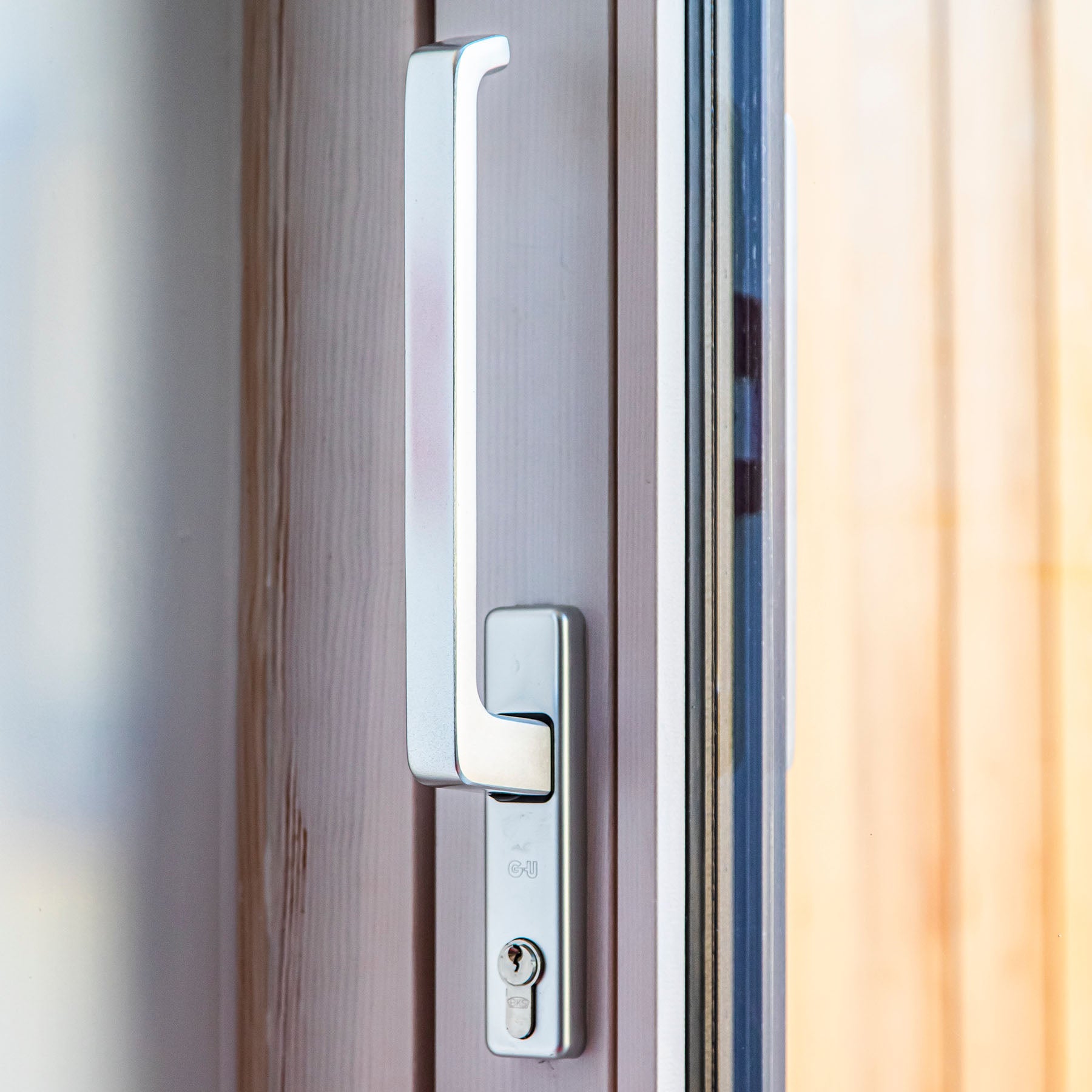 Close-up of a modern door handle on a triple-glazed wooden door with a blurred background