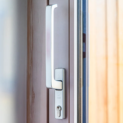 Close-up of a modern door handle on a triple-glazed wooden door with a blurred background