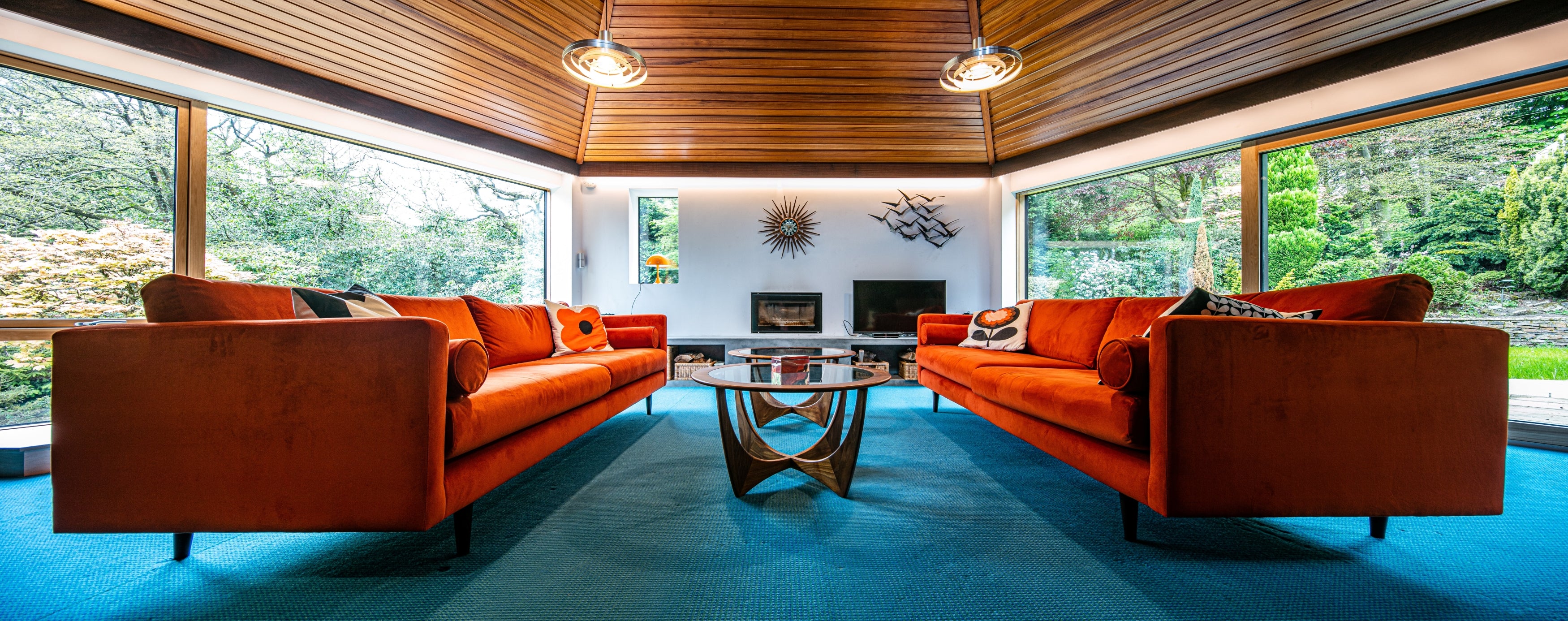 Passive house modern living room with orange sofas, a glass coffee table, and large triple-glazed windows.
