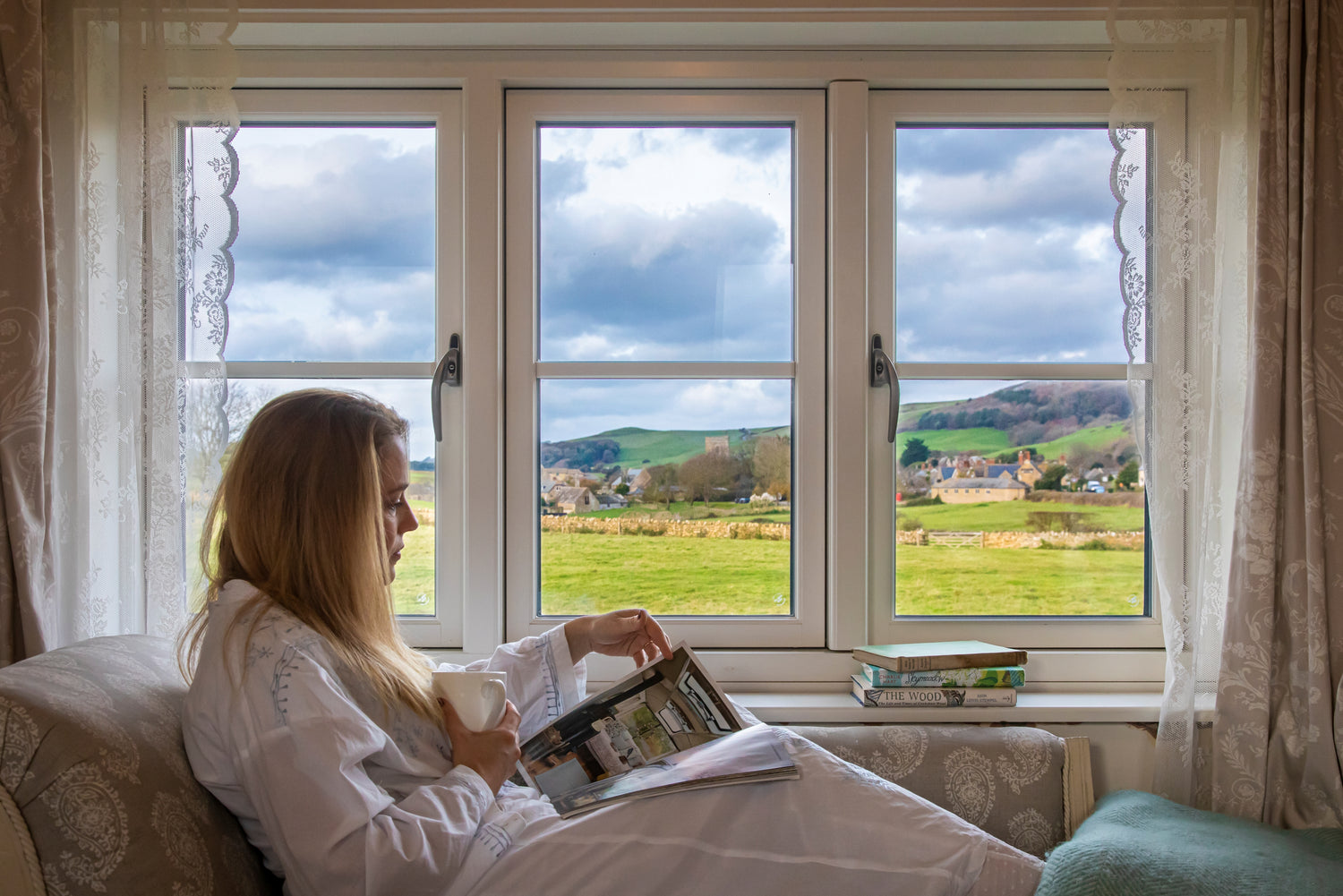 Woman reading a book by a triple-glazed window with a scenic view