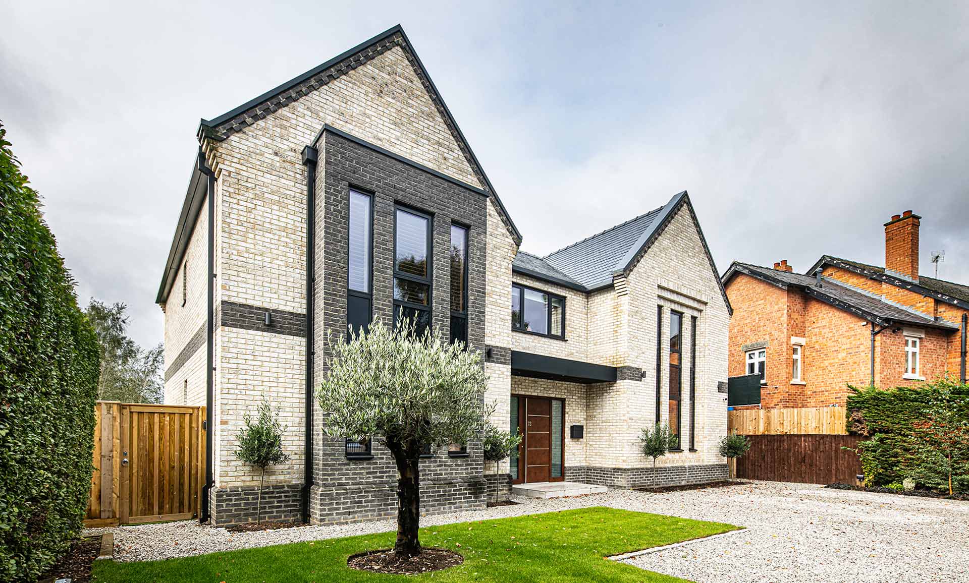 Image of a modern, grey and sand-coloured brick new build house with tall, dark composite windows across the whole front elevation